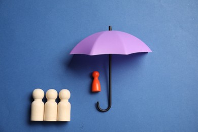 Photo of Human figures under umbrella on blue background, top view. Insurance concept