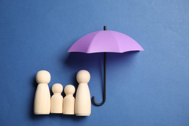 Photo of Human figures under umbrella on blue background, top view. Insurance concept