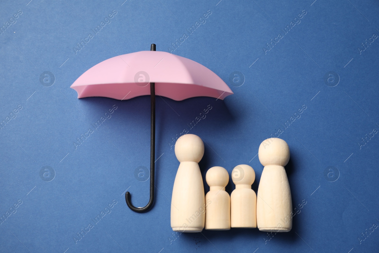 Photo of Human figures under umbrella on blue background, top view. Insurance concept