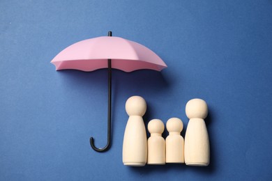 Photo of Human figures under umbrella on blue background, top view. Insurance concept