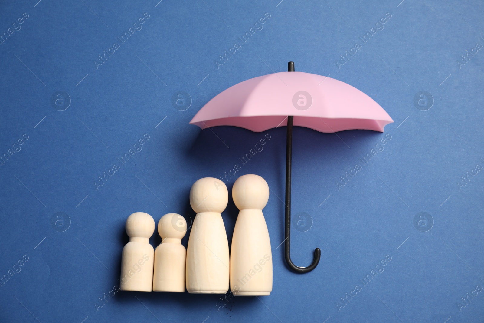 Photo of Human figures under umbrella on blue background, top view. Insurance concept