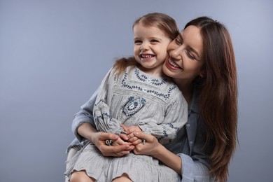 Happy mother with her cute little daughter on grey background