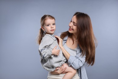 Happy mother with her cute little daughter on grey background