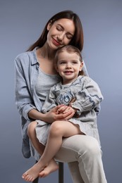 Happy mother with her cute little daughter on grey background