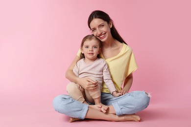 Happy mother with her cute little daughter on pink background