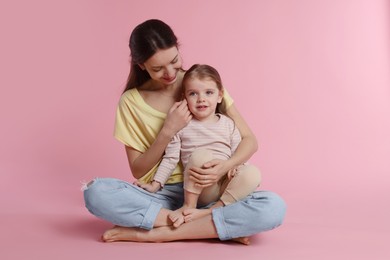 Happy mother with her cute little daughter on pink background