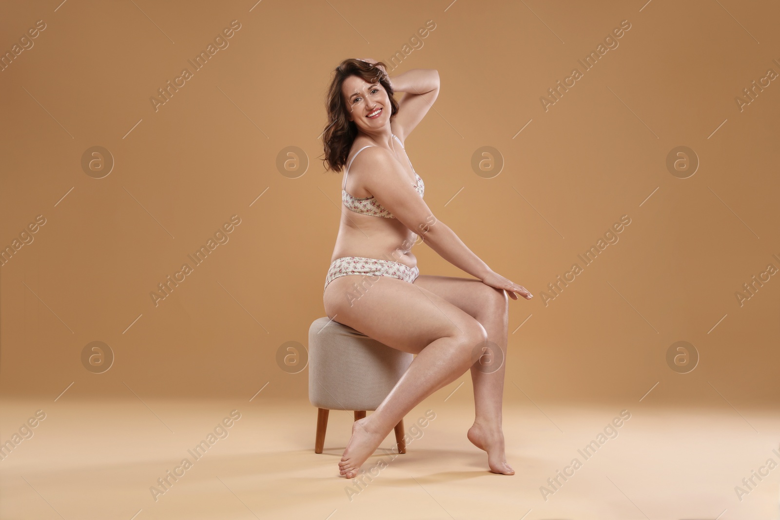 Photo of Beautiful woman in underwear on pouf against dark beige background. Cellulite problem