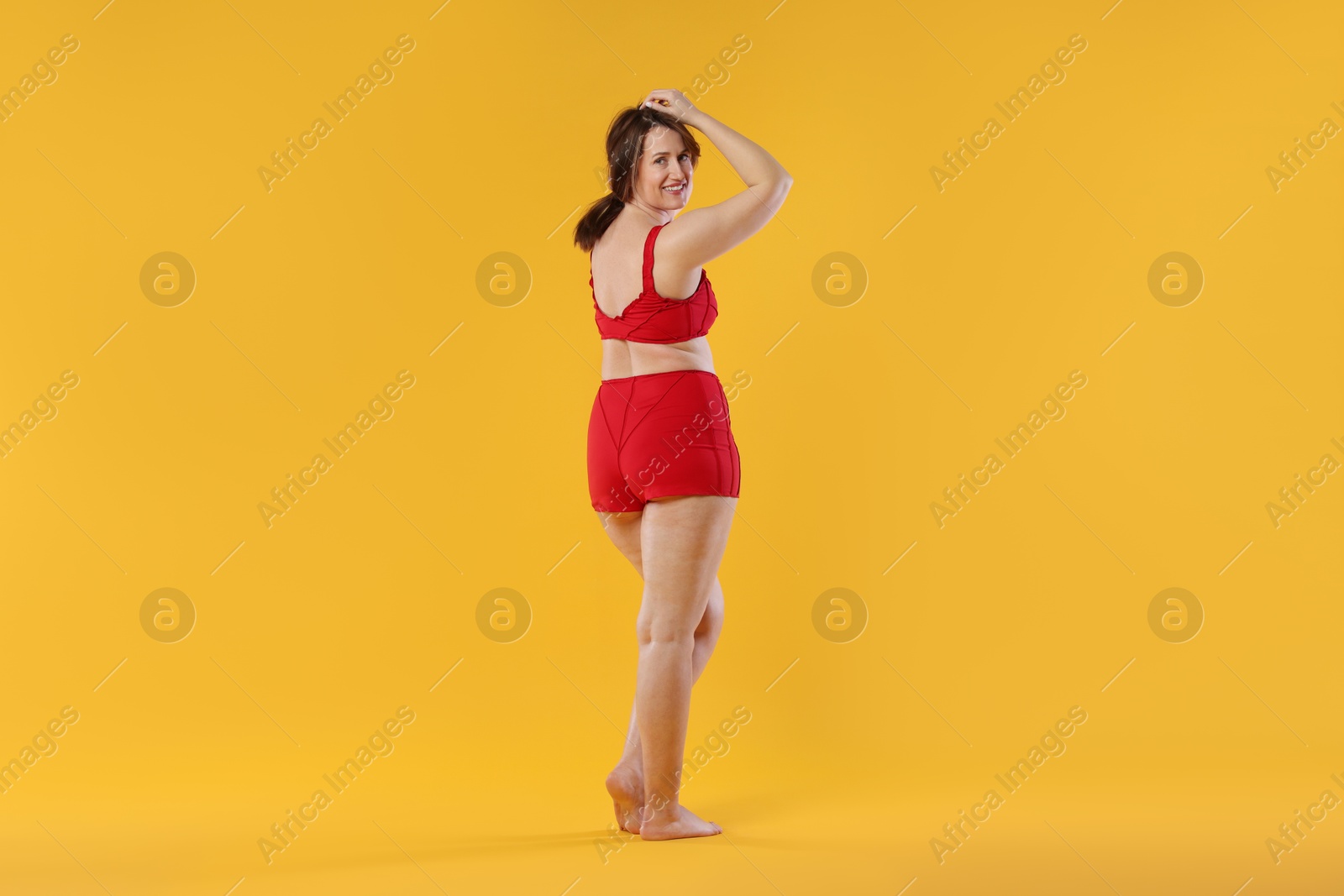 Photo of Woman in red underwear on orange background. Cellulite problem