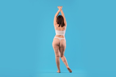 Woman in underwear on light blue background, back view. Cellulite problem