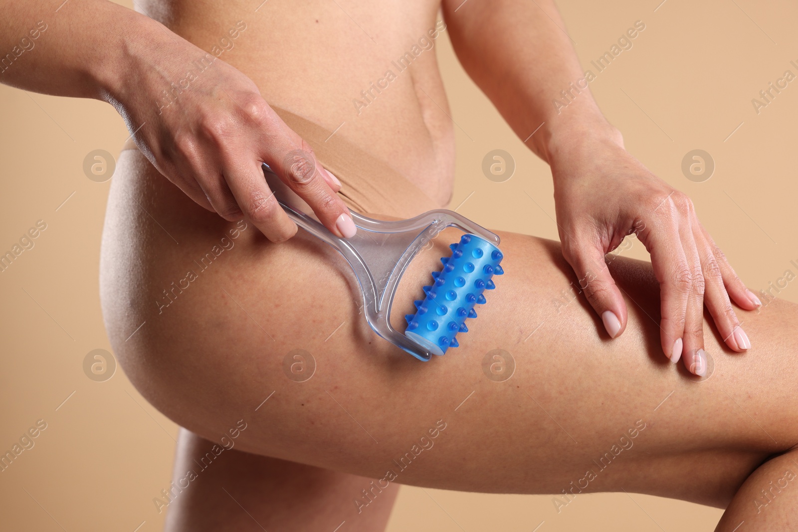 Photo of Woman doing anti cellulite massage with roller on beige background, closeup