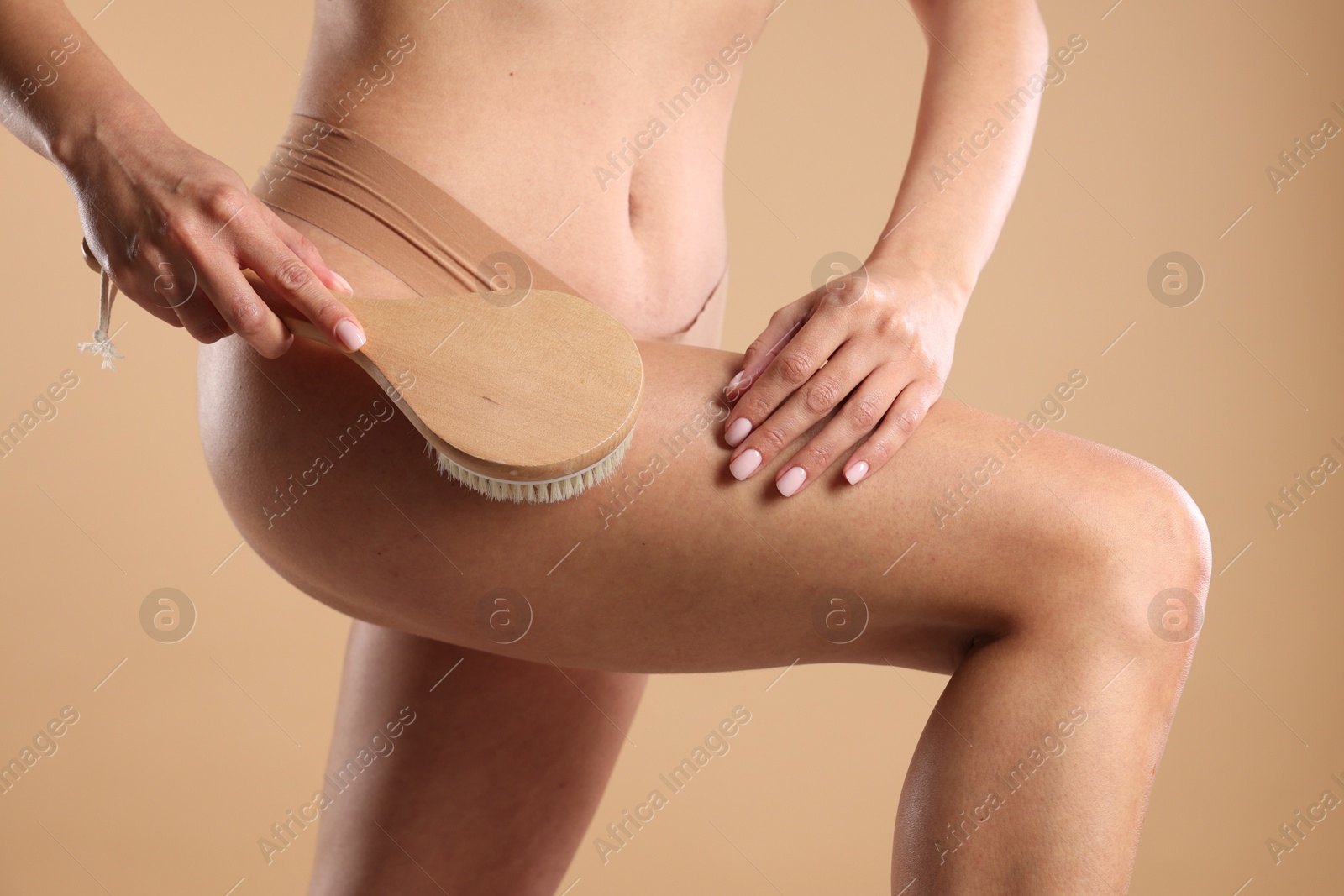 Photo of Woman doing anti cellulite massage with brush on beige background, closeup