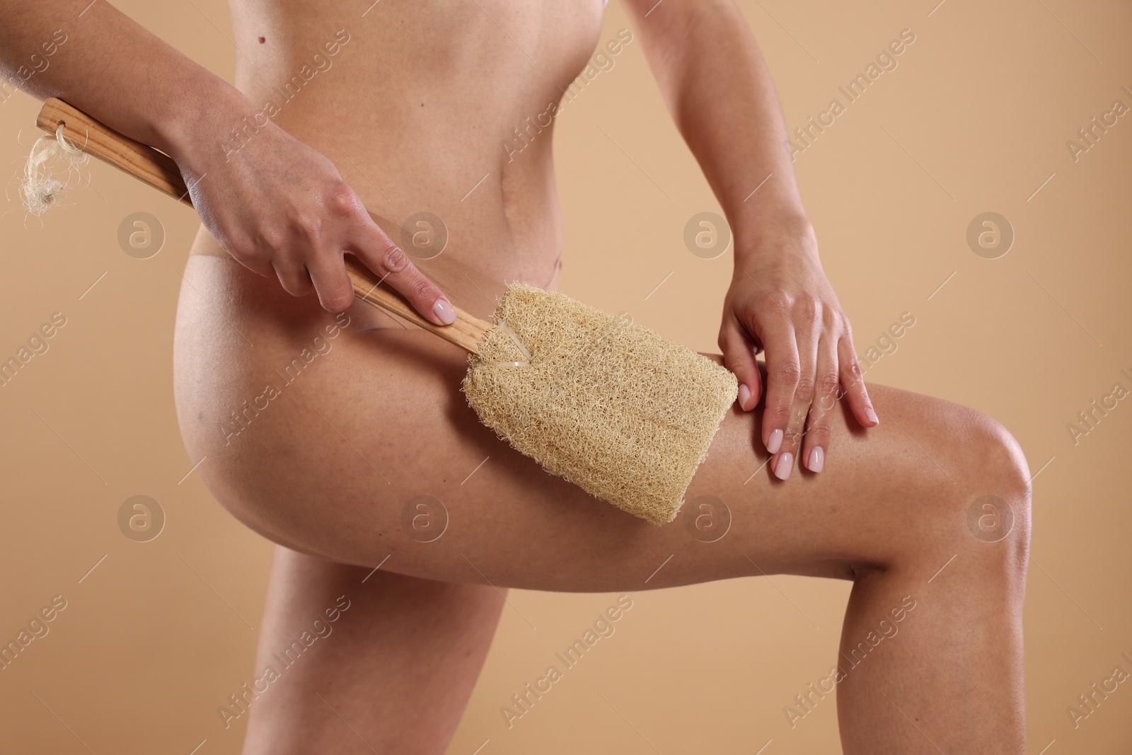 Photo of Woman doing anti cellulite massage with loofah on beige background, closeup