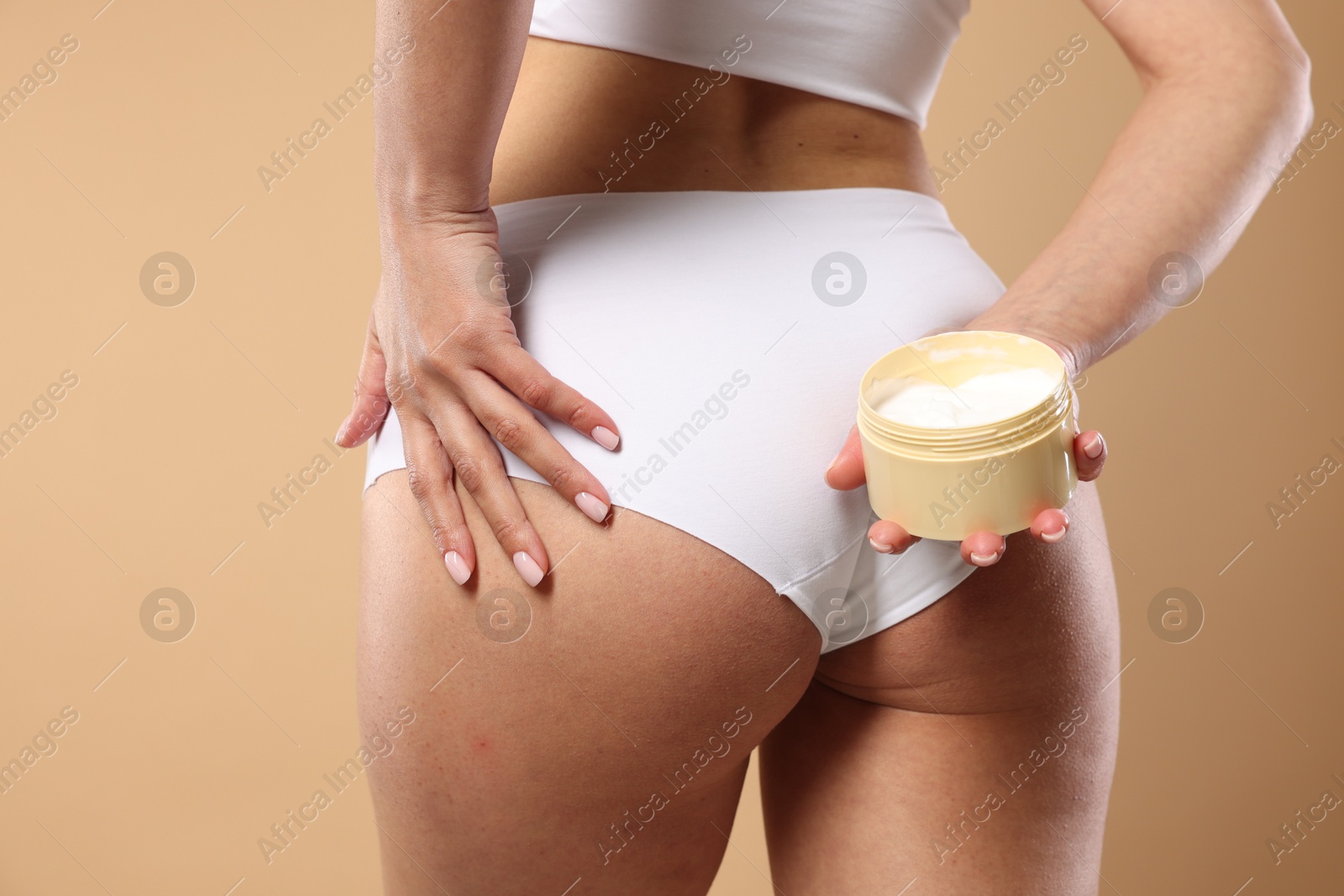 Photo of Woman applying anti cellulite cream on beige background, closeup