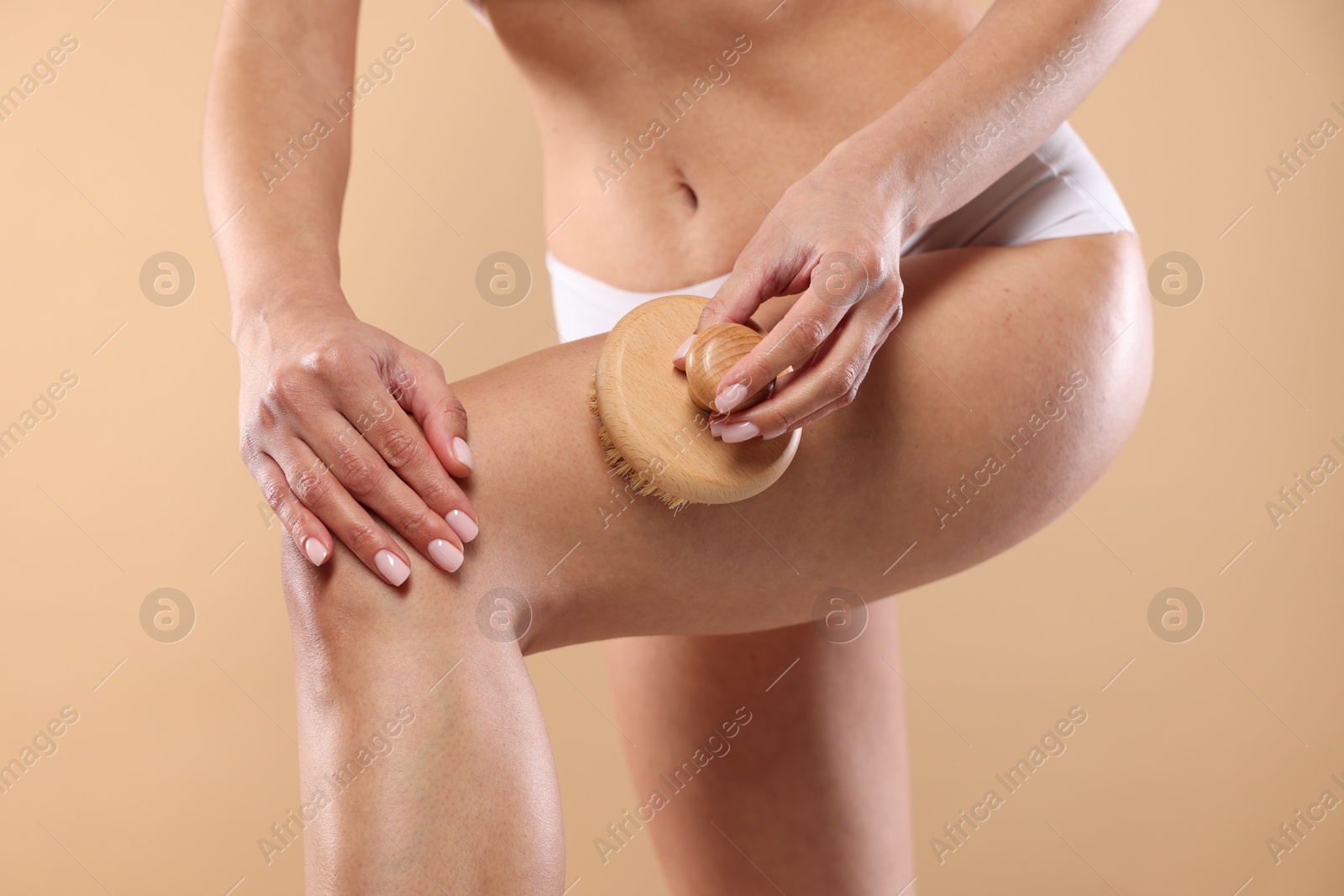 Photo of Woman doing anti cellulite massage with brush on beige background, closeup