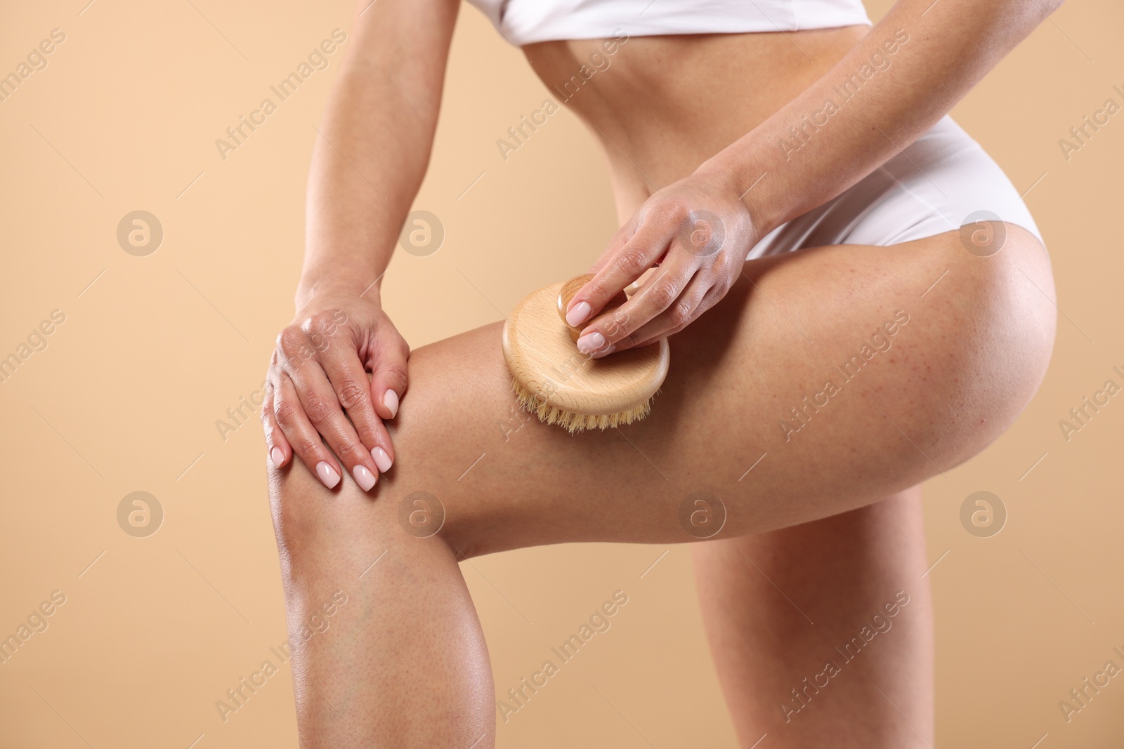 Photo of Woman doing anti cellulite massage with brush on beige background, closeup