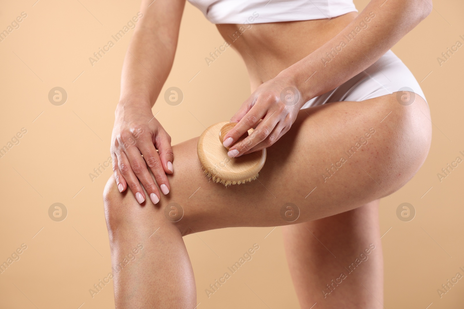 Photo of Woman doing anti cellulite massage with brush on beige background, closeup