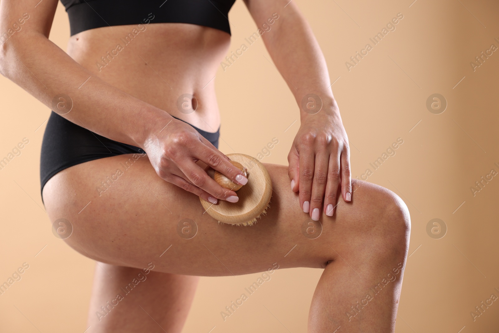 Photo of Woman doing anti cellulite massage with brush on beige background, closeup