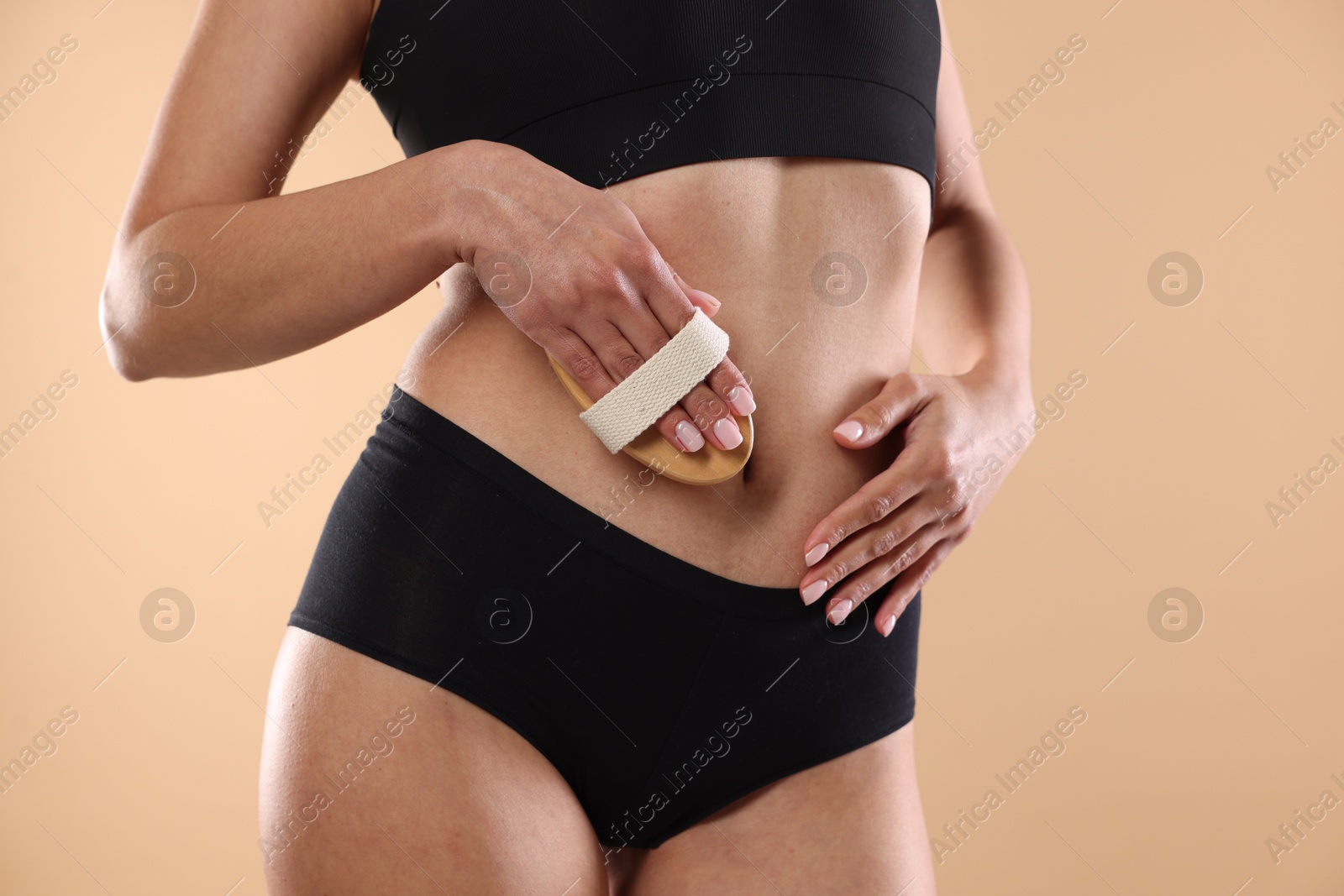 Photo of Woman doing anti cellulite massage with brush on beige background, closeup