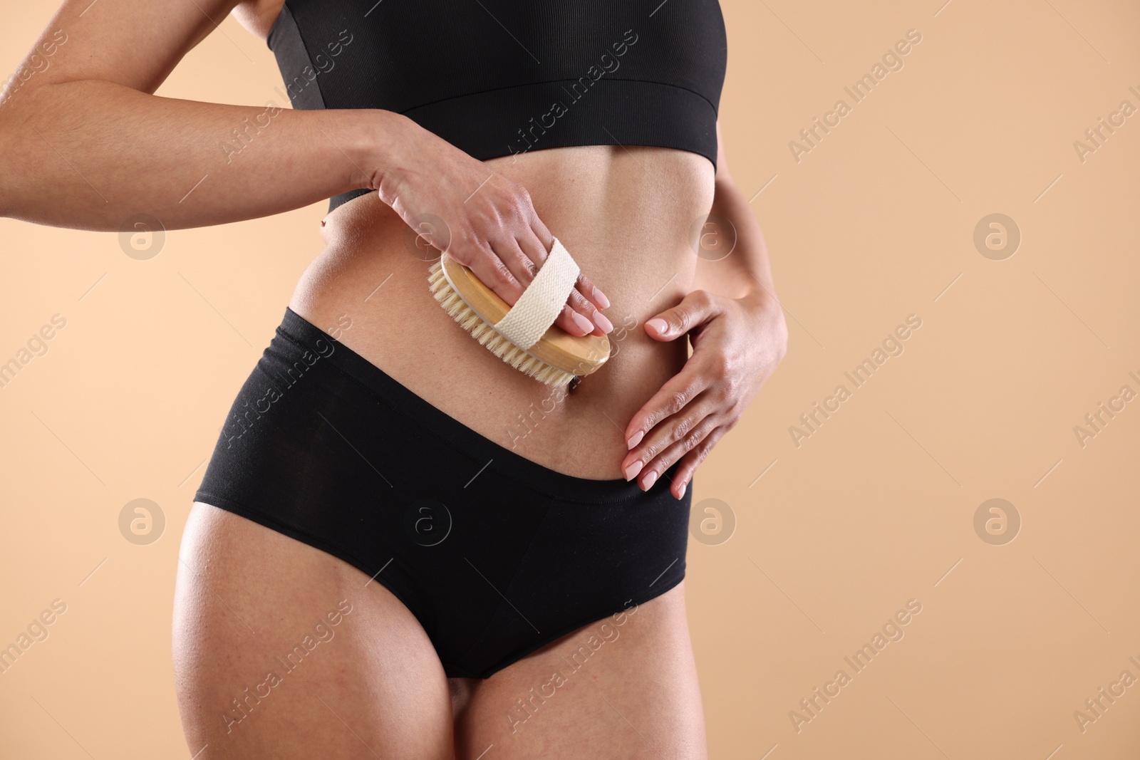 Photo of Woman doing anti cellulite massage with brush on beige background, closeup