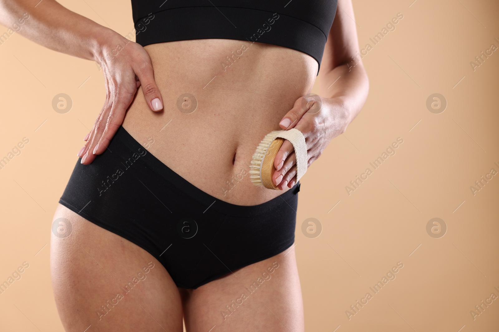 Photo of Woman doing anti cellulite massage with brush on beige background, closeup