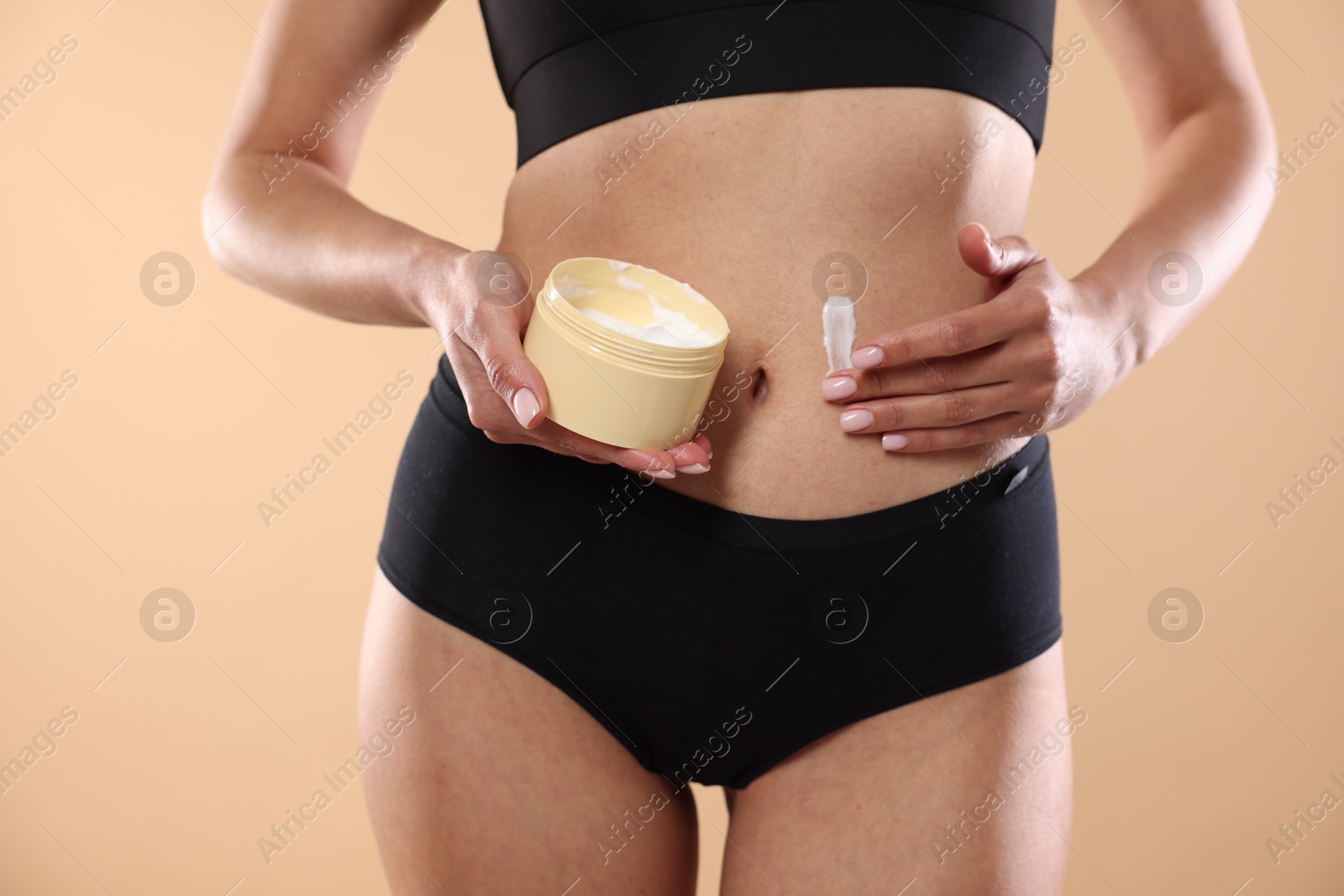 Photo of Woman applying anti cellulite cream on beige background, closeup