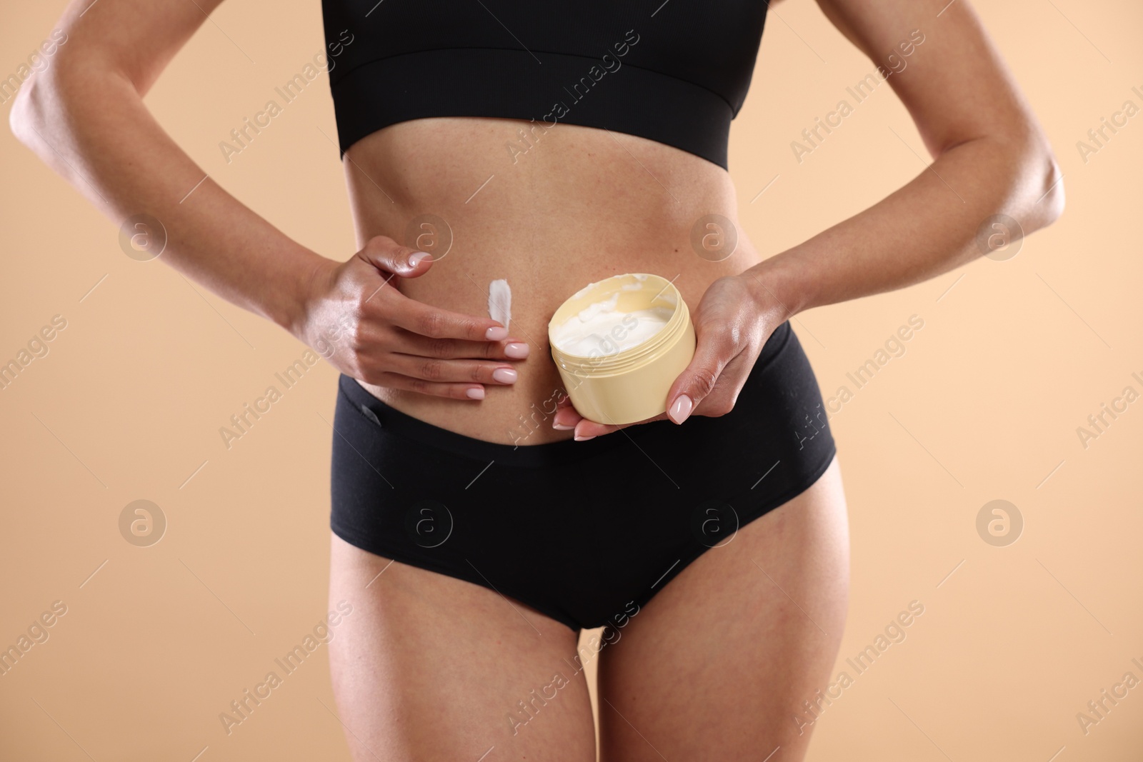 Photo of Woman applying anti cellulite cream on beige background, closeup