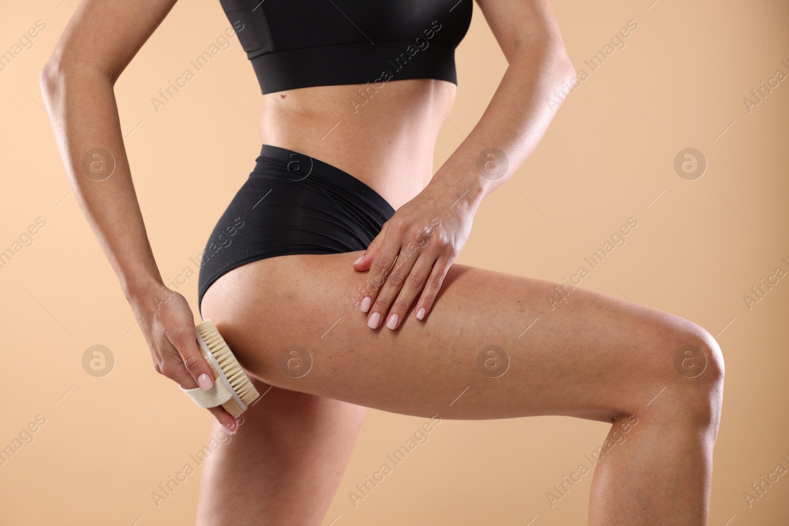 Photo of Woman doing anti cellulite massage with brush on beige background, closeup