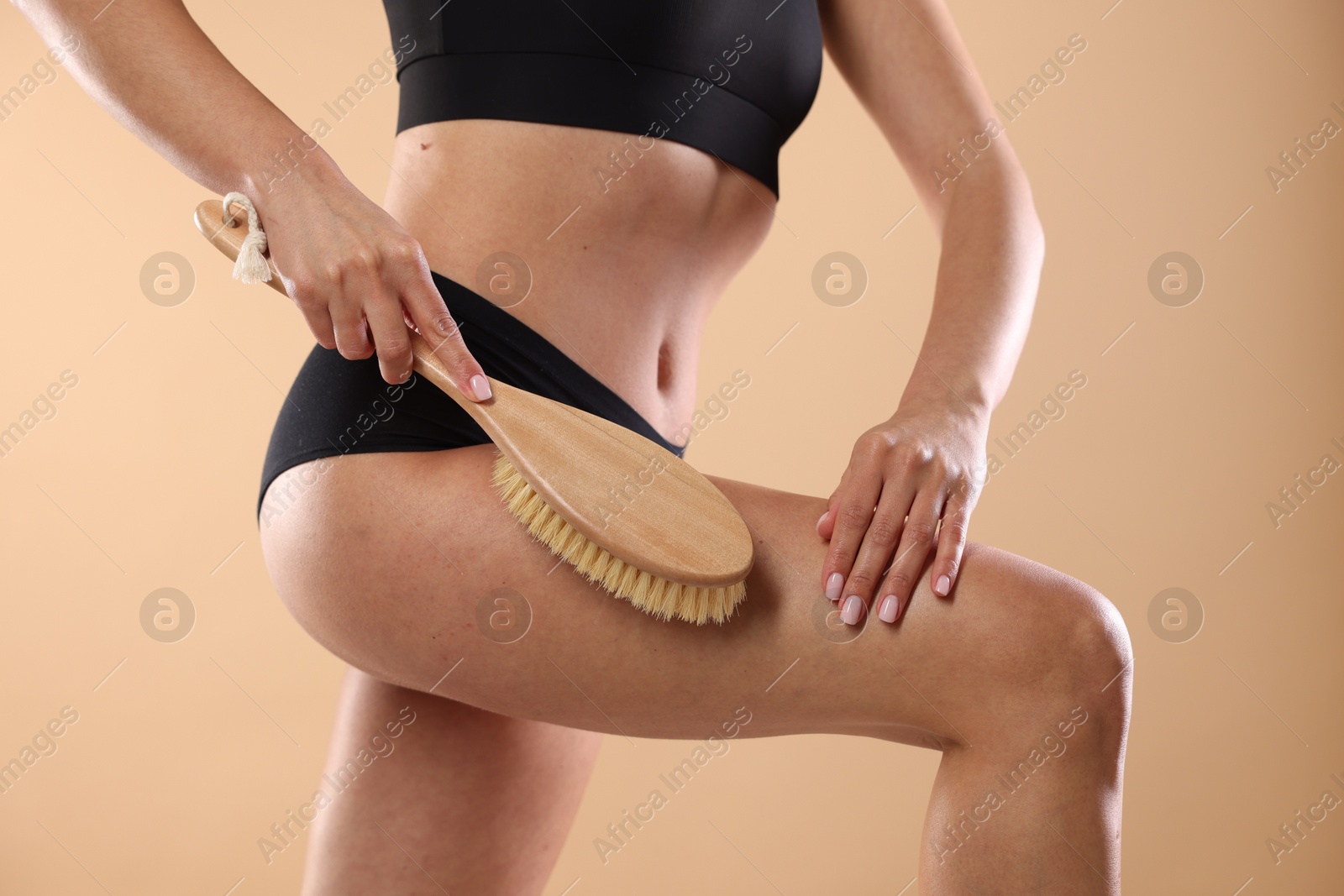 Photo of Woman doing anti cellulite massage with brush on beige background, closeup