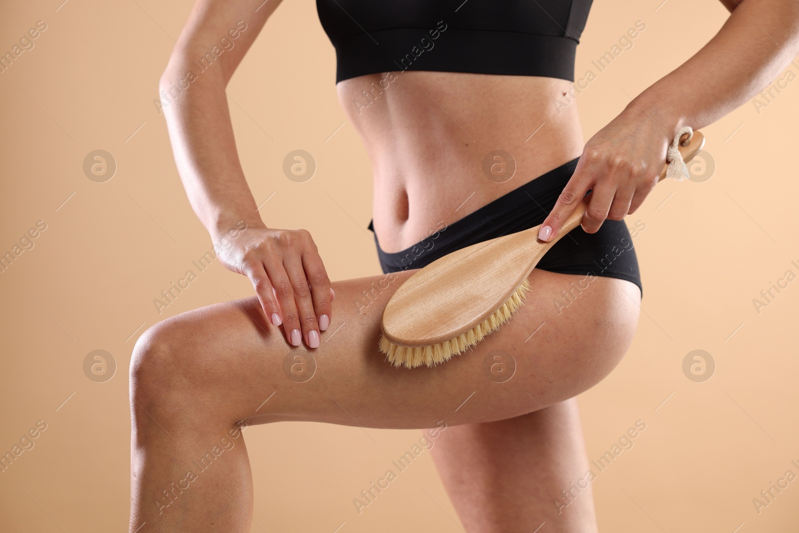 Photo of Woman doing anti cellulite massage with brush on beige background, closeup