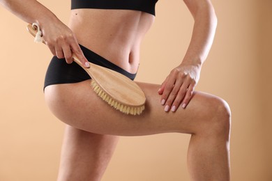 Photo of Woman doing anti cellulite massage with brush on beige background, closeup