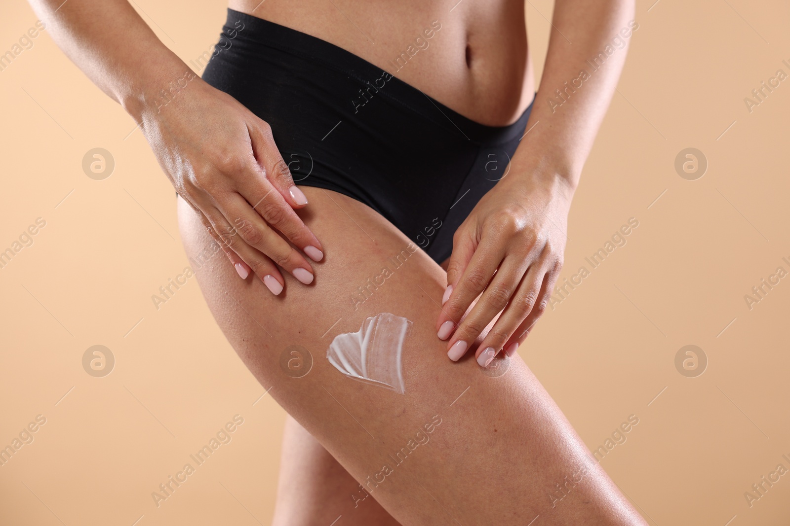 Photo of Woman applying anti cellulite cream on beige background, closeup