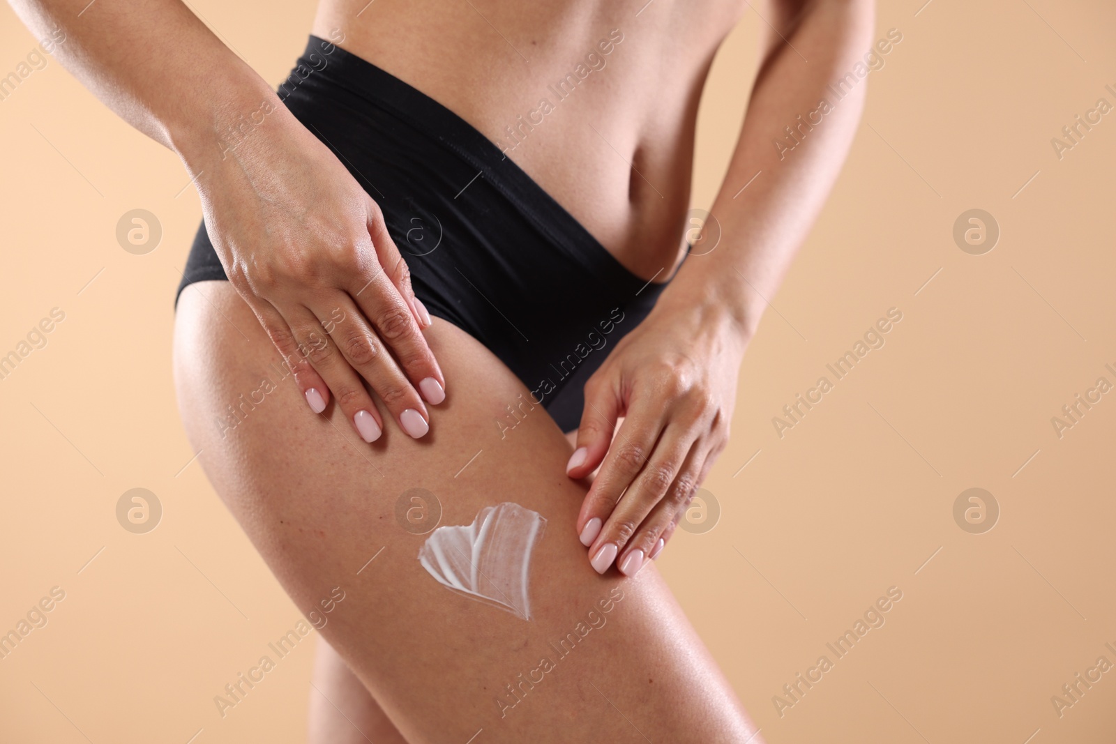 Photo of Woman applying anti cellulite cream on beige background, closeup