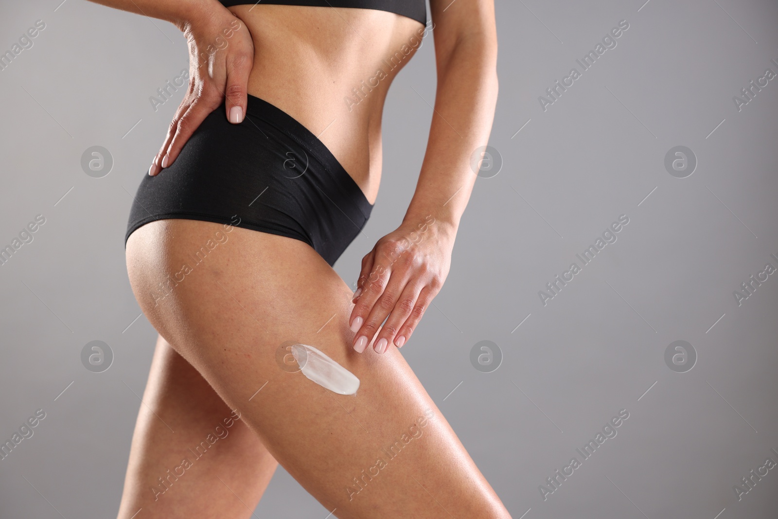 Photo of Woman applying anti cellulite cream on grey background, closeup