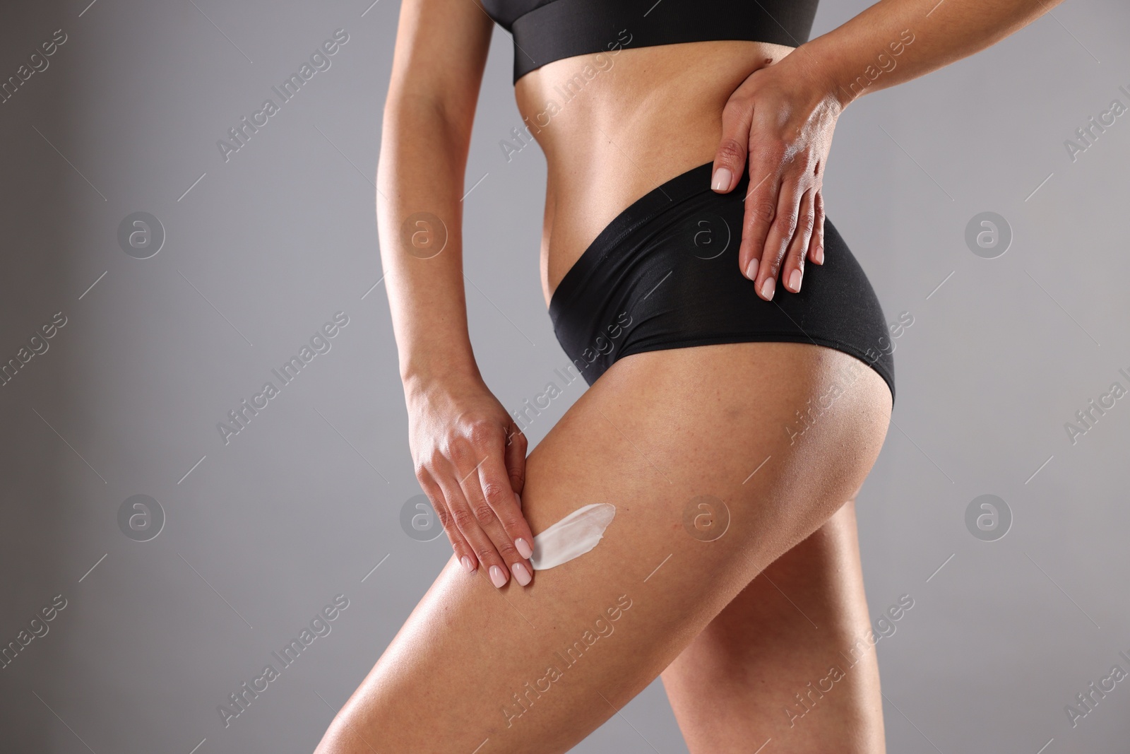 Photo of Woman applying anti cellulite cream on grey background, closeup