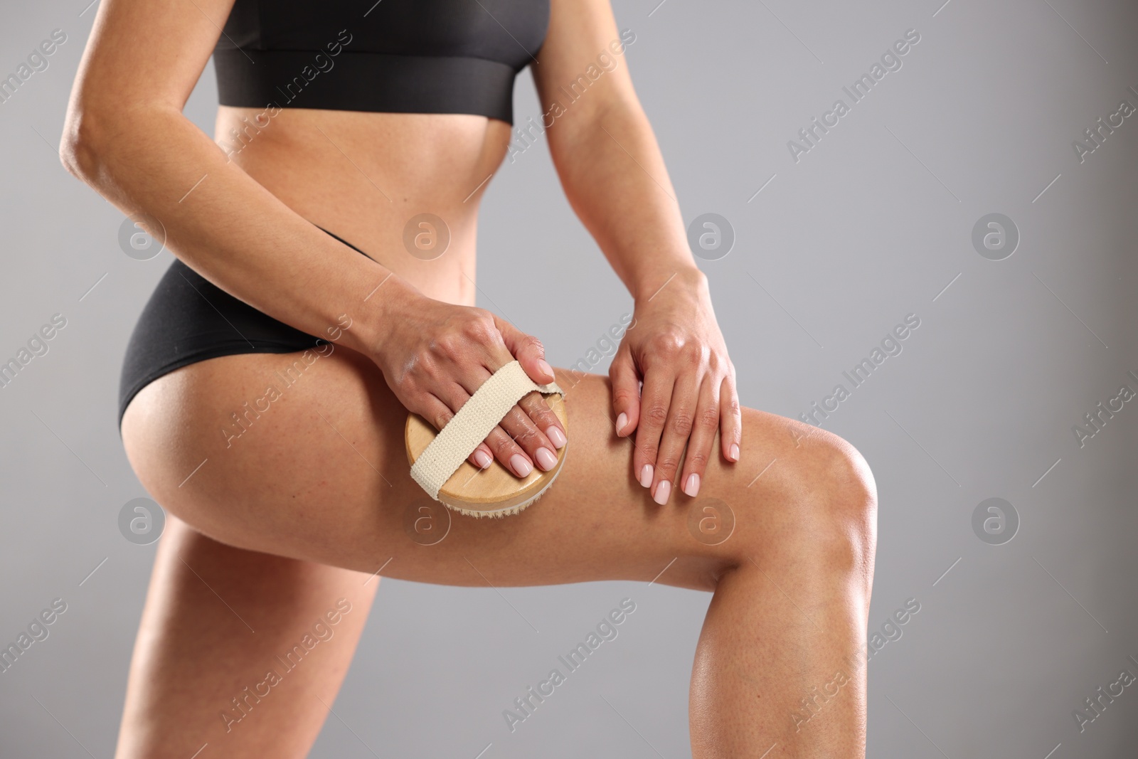 Photo of Woman doing anti cellulite massage with brush on grey background, closeup