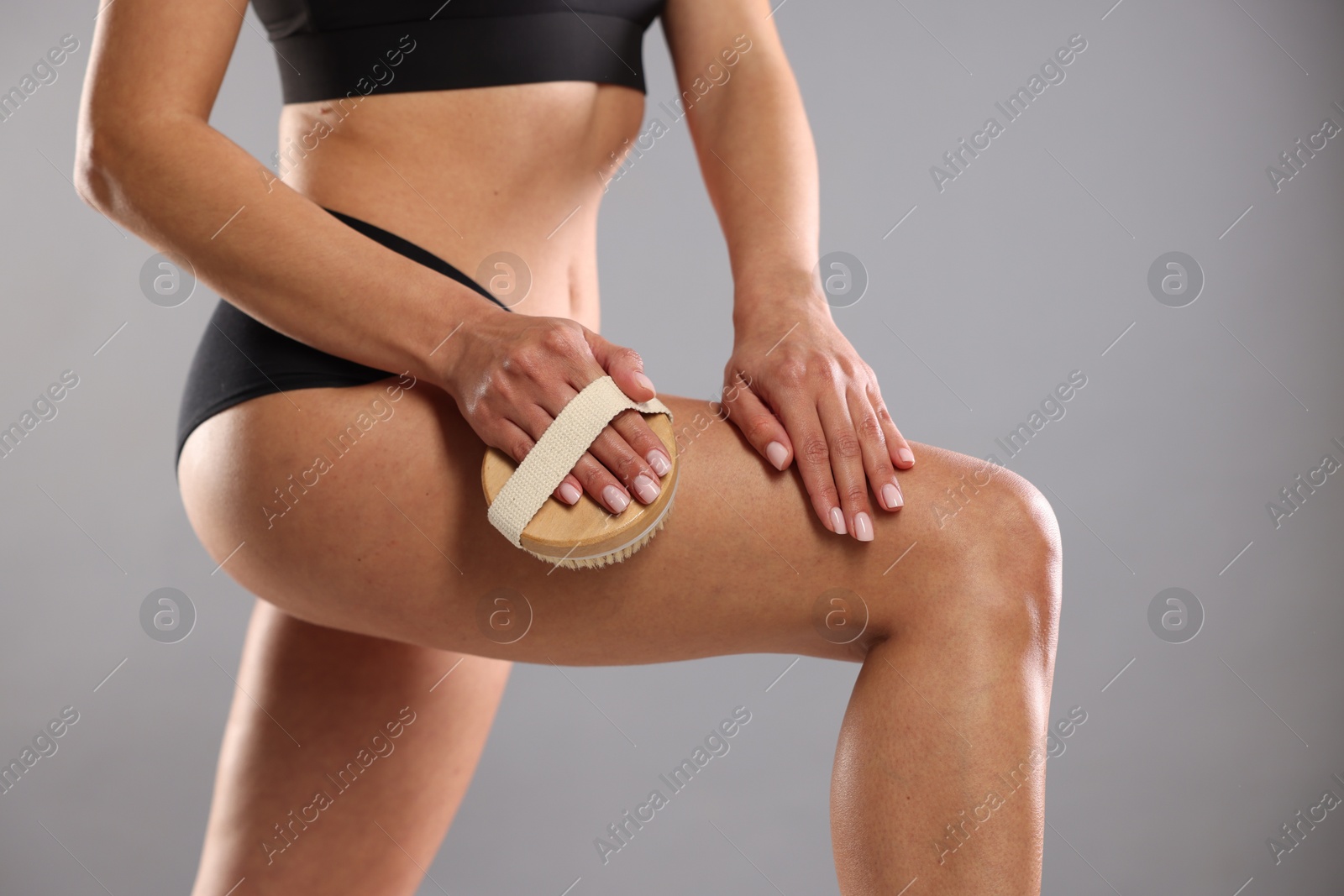 Photo of Woman doing anti cellulite massage with brush on grey background, closeup