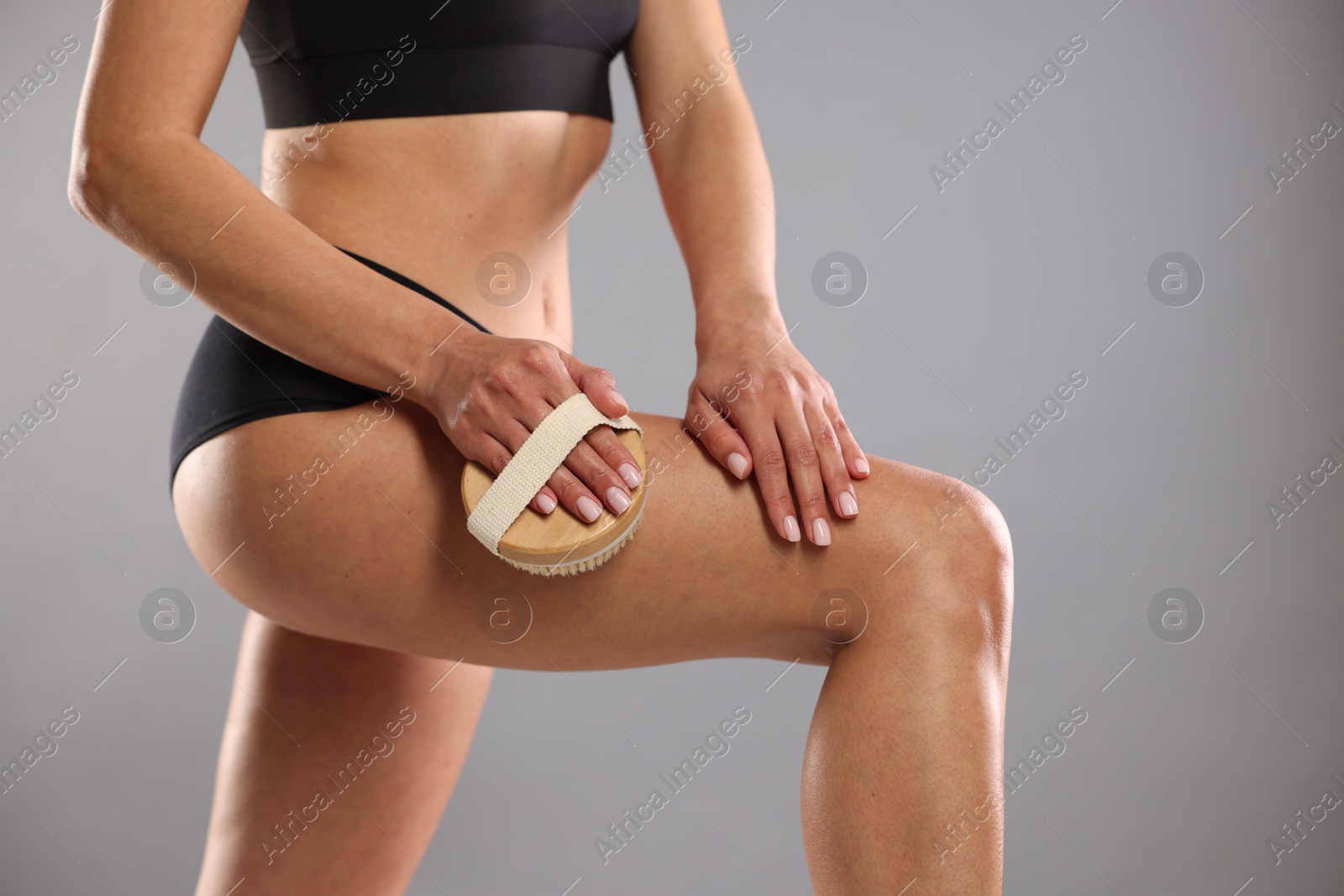 Photo of Woman doing anti cellulite massage with brush on grey background, closeup