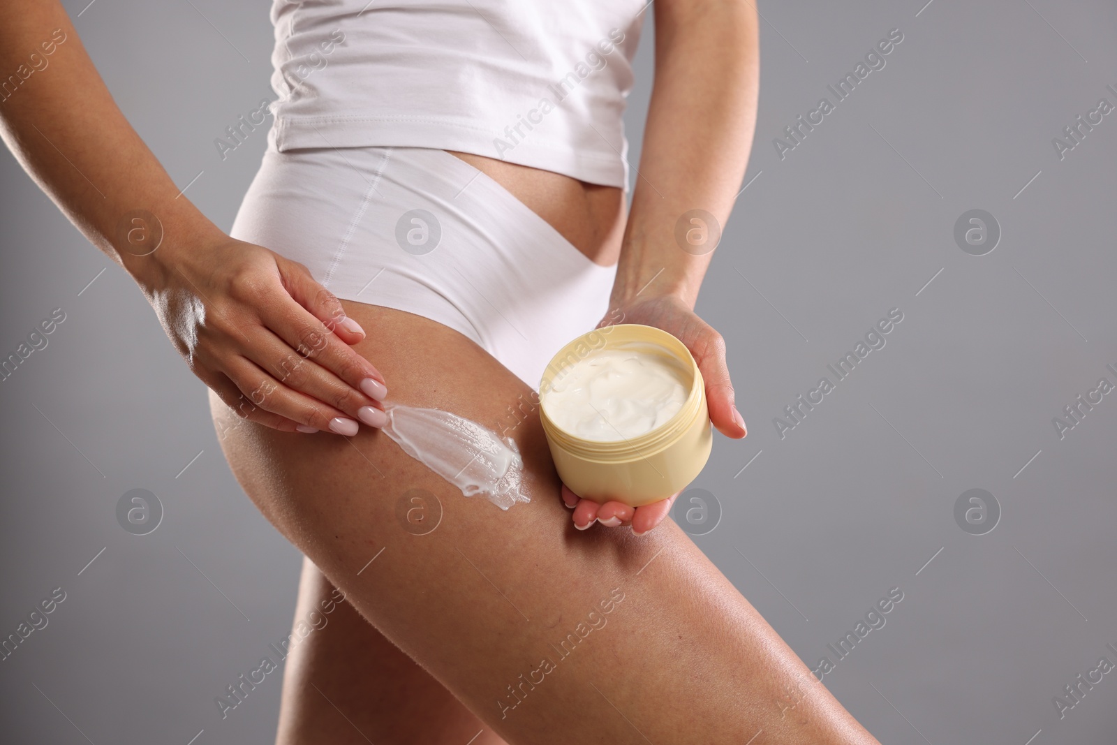 Photo of Woman applying anti cellulite cream on grey background, closeup