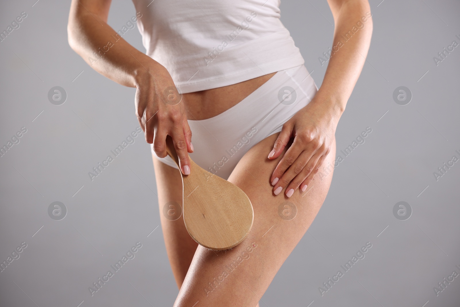 Photo of Woman doing anti cellulite massage with brush on grey background, closeup