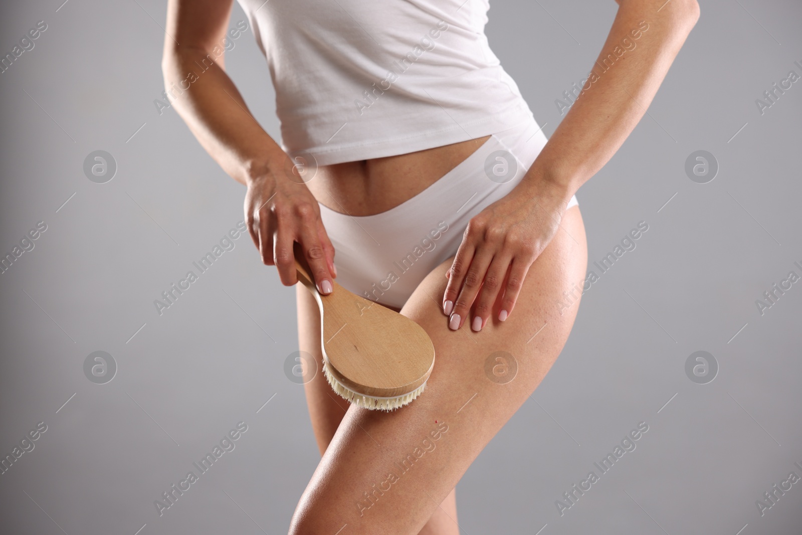 Photo of Woman doing anti cellulite massage with brush on grey background, closeup