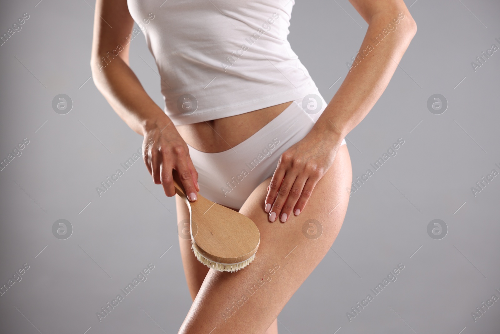 Photo of Woman doing anti cellulite massage with brush on grey background, closeup