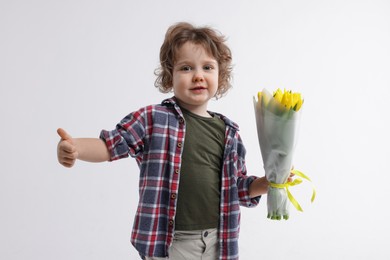 Photo of Cute little boy with bouquet of tulips showing thumbs up on white background