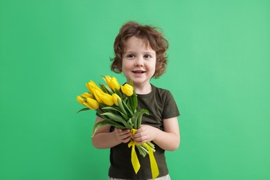 Photo of Cute little boy with bouquet of tulips on green background