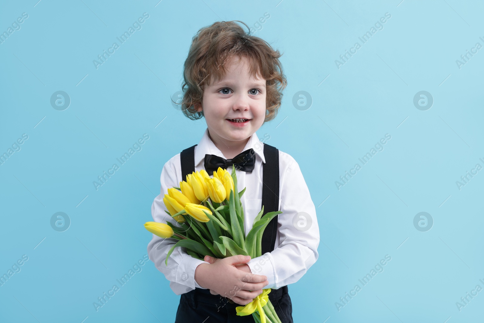 Photo of Cute little boy with bouquet of tulips on light blue background