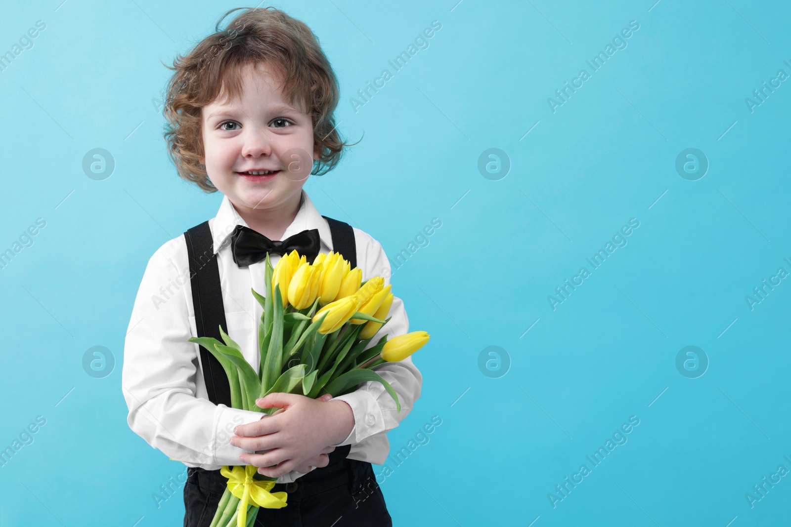 Photo of Cute little boy with bouquet of tulips on light blue background. Space for text