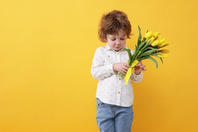 Cute little boy with bouquet of tulips on yellow background. Space for text