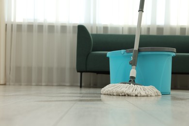 Photo of String mop and bucket on floor indoors, space for text