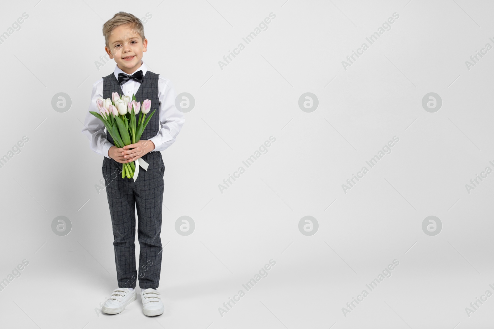 Photo of Cute little boy with bouquet of tulips on white background. Space for text