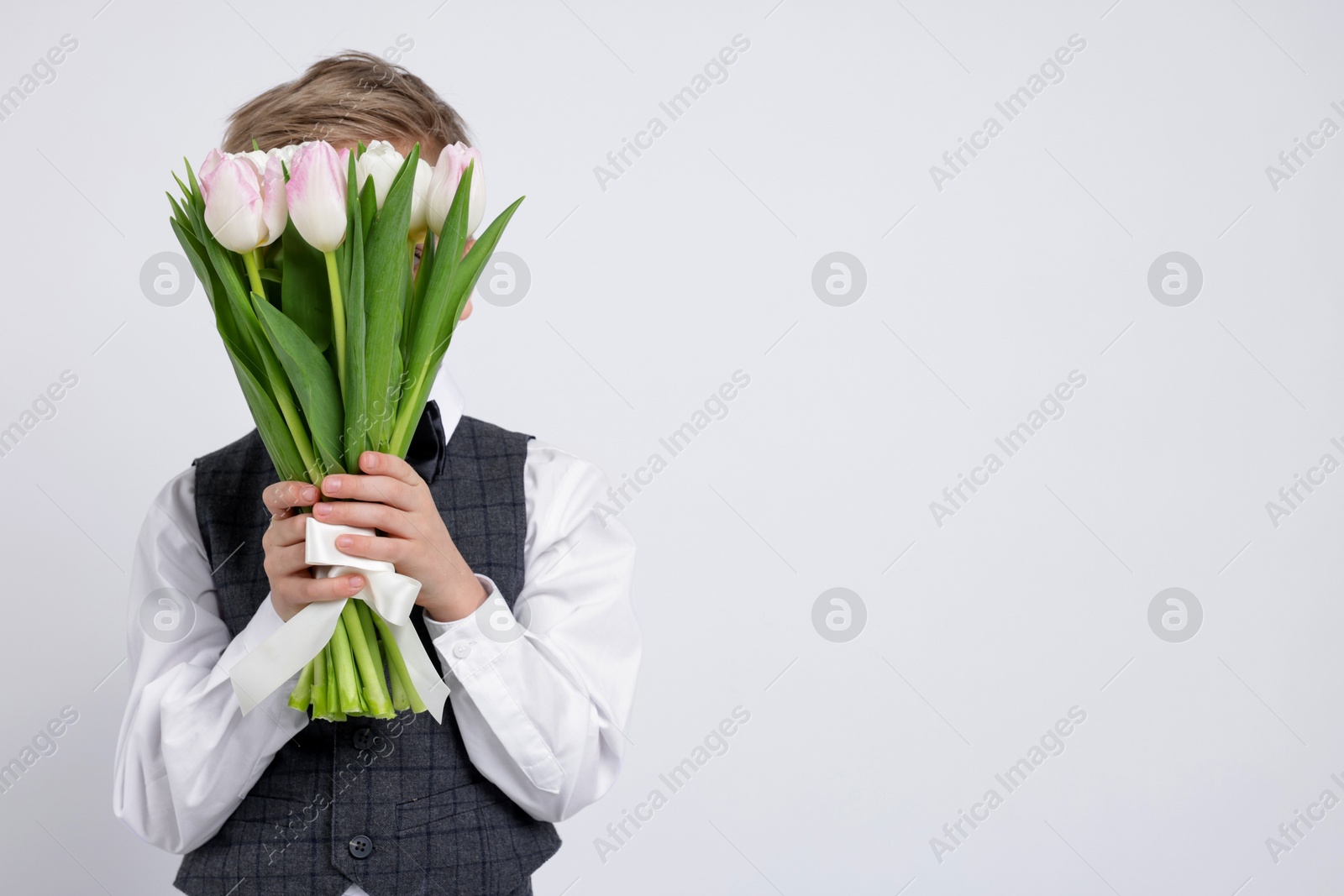 Photo of Little boy hiding behind bouquet of tulips on white background. Space for text