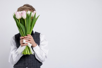 Little boy hiding behind bouquet of tulips on white background. Space for text